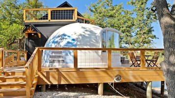 Une structure sphérique dotée d’une terrasse en bois et d’un escalier menant à une maison dont le toit est noir.