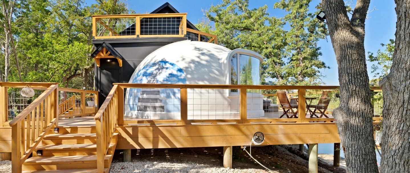 Eine kugelförmige Struktur mit einer Holzdielen-Terrasse und Treppen, die zu einem Haus mit schwarzem Dach führen.