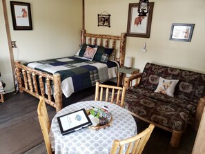 Una habitación acogedora con una cama de madera, un sofá, una mesa redonda con una tablet y una silla pequeña.