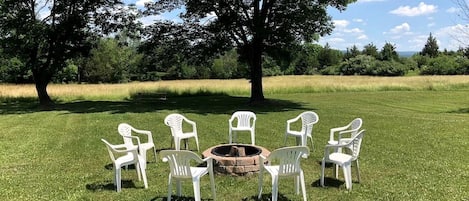 Un espacio al aire libre con césped, con un círculo de sillas de plástico blancas alrededor de una chimenea central.