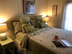 A neatly made bed with pillows, a bedside lamp, a framed picture on the wall, and a window with curtains. - Wine Country Cottage Overlooking the Lake in Starkey, New York (Starkey)