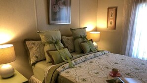 Ein ordentlich bezogenes Bett mit Kissen, eine Nachttischlampe, ein gerahmtes Bild an der Wand und ein Fenster mit Vorhängen.
