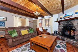 A cozy living room with a fireplace, wooden ceiling beams, and a leather sofa. - Cute Cabin with Fireplace and Private Patio in Big Bear Lake, California (Big Bear Lake)