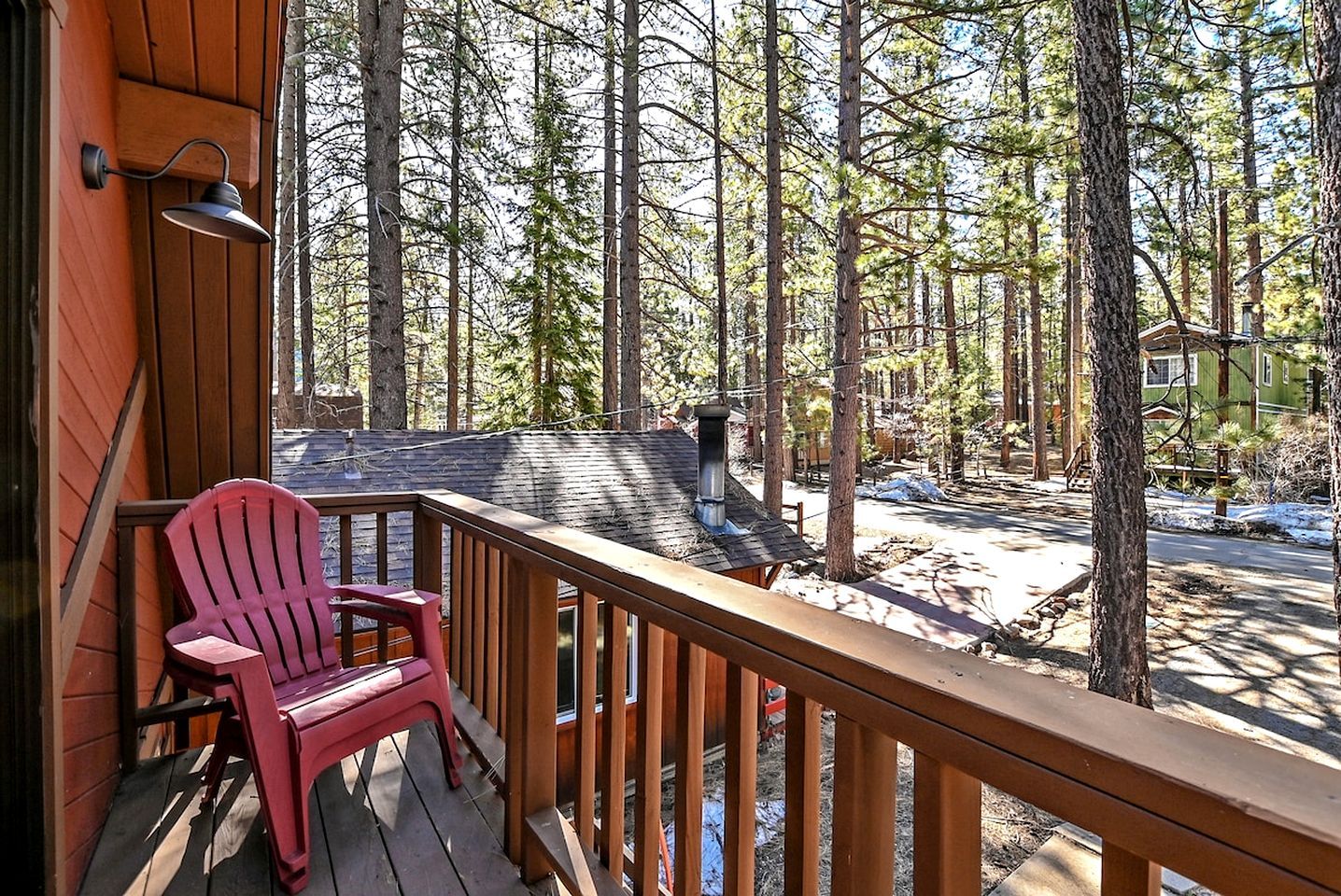 A wooden deck with a red chair, surrounded by a forest with tall trees.
