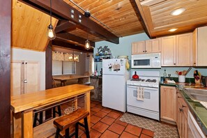 A kitchen with wooden cabinets, a dining table, and a stove. - Cute Cabin with Fireplace and Private Patio in Big Bear Lake, California (Big Bear Lake)
