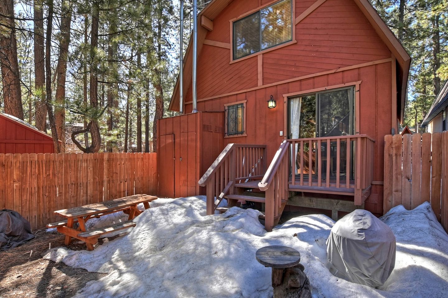 A cabin with a wooden deck, a covered picnic table, and a staircase leading to a second-story window.