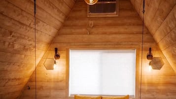 A cozy attic bedroom with a bed, hanging light fixtures, and a window.