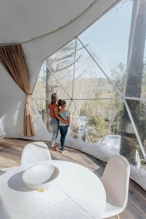 Una estructura de cúpula geodésica con un ventanal grande, una mesa blanca y una silla.