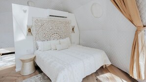 A bedroom with a white bed, a round bedside table, and a headboard with a decorative pattern. - Unmatched Views Await You at this Cherry Log, Georgia Designer Dome near Fall Branch Falls (Cherry Log)