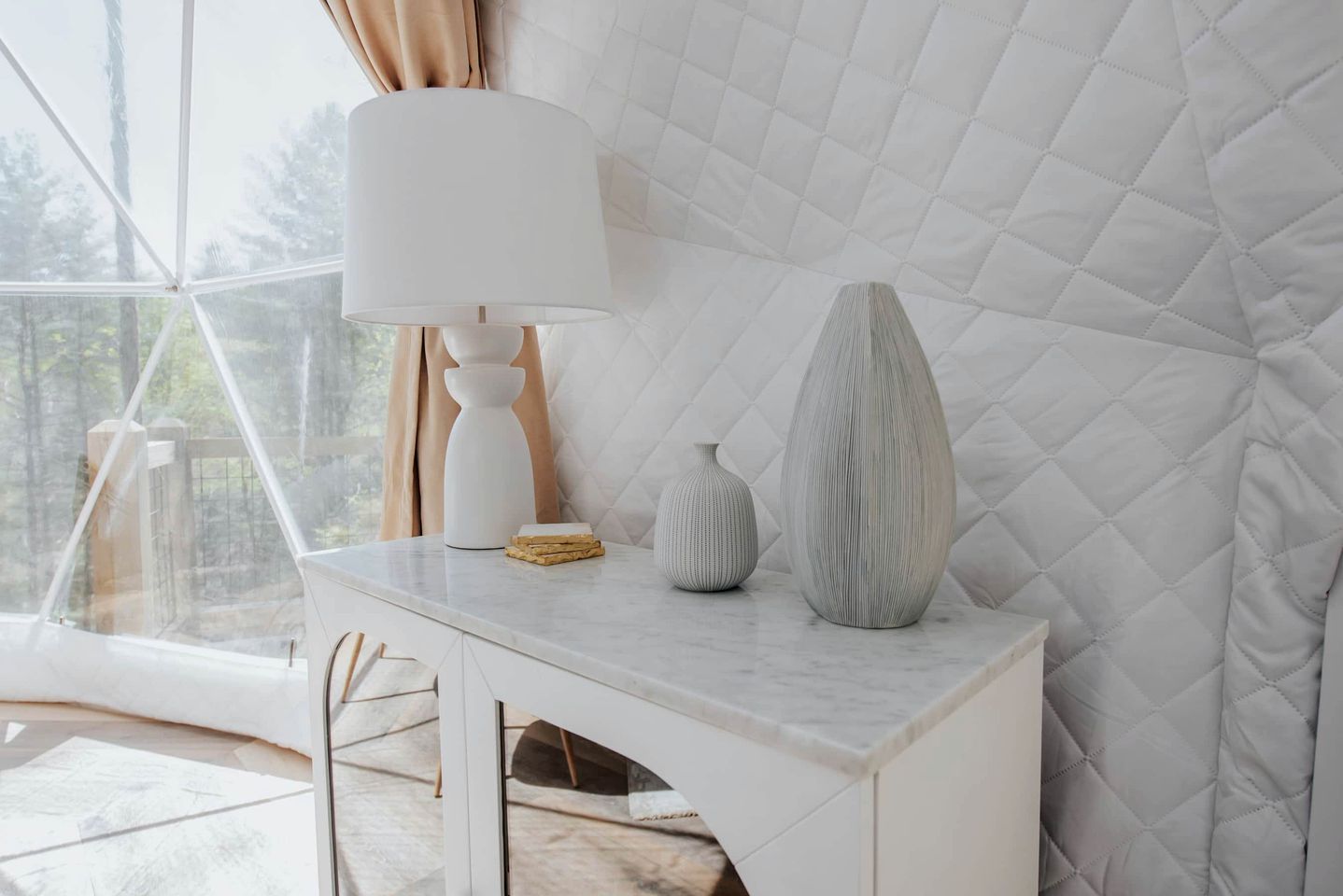 A modern room with a large window, a white table with a lamp, and two decorative vases.