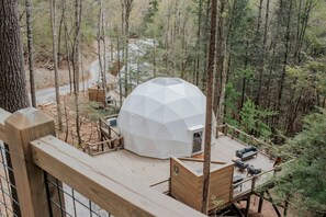 Une structure en forme de dôme géodésique dotée d’une terrasse et d’un espace extérieur aménagé pour s’asseoir, le tout entouré d’une forêt.