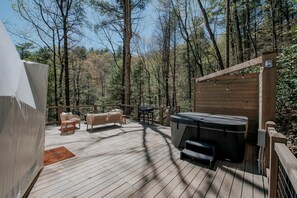 Una terraza de madera con un jacuzzi, mobiliario de mimbre y una tienda de campaña.