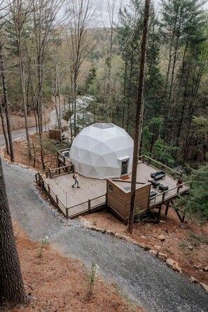 A geodesic dome structure with a wooden deck and outdoor seating area surrounded by forest. - Unmatched Views Await You at this Cherry Log, Georgia Designer Dome near Fall Branch Falls (Cherry Log)