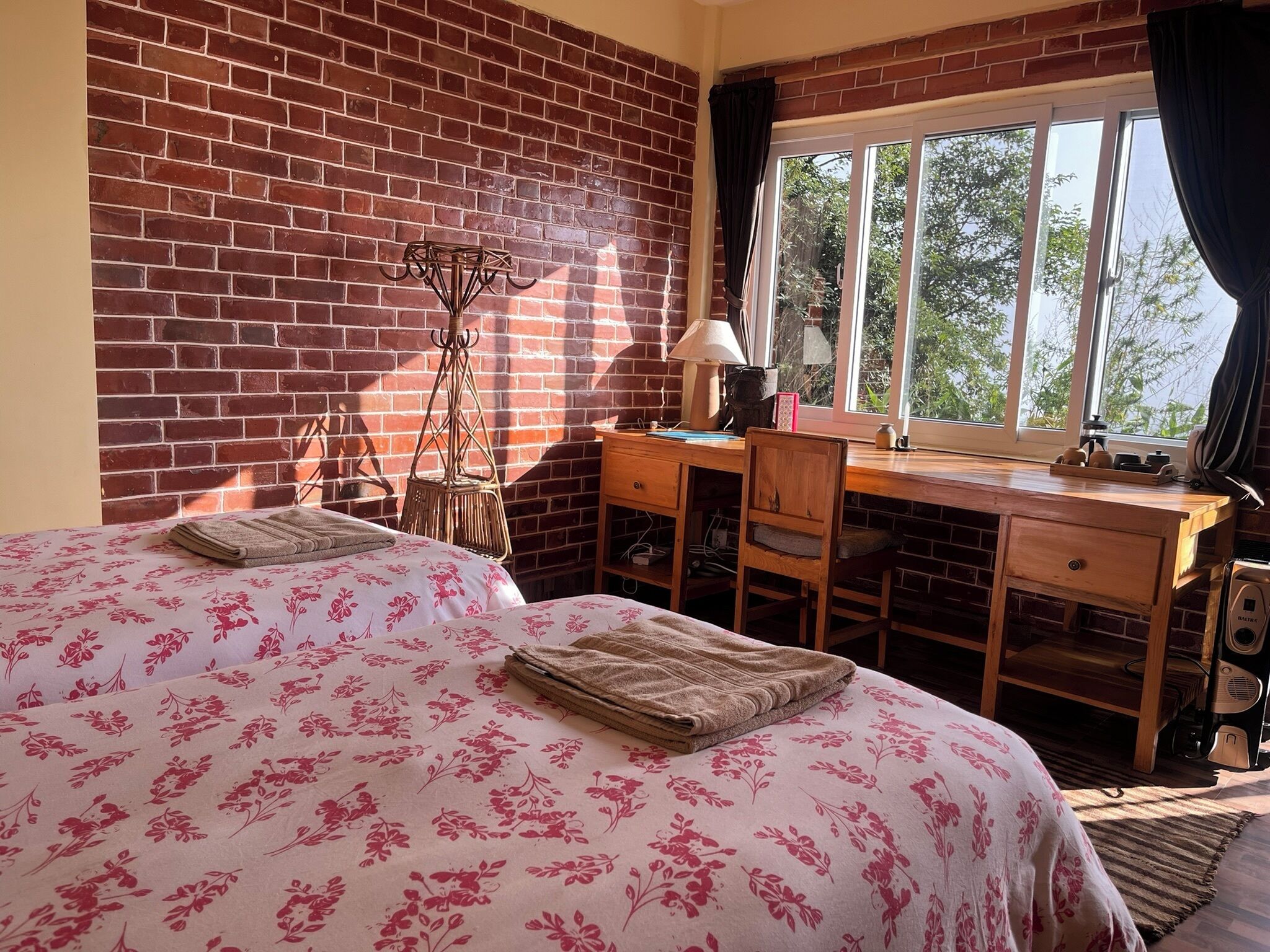 Een kamer met twee bedden, een bureau en een stoel. Er is een raam met gordijnen, een lamp en een radiator.