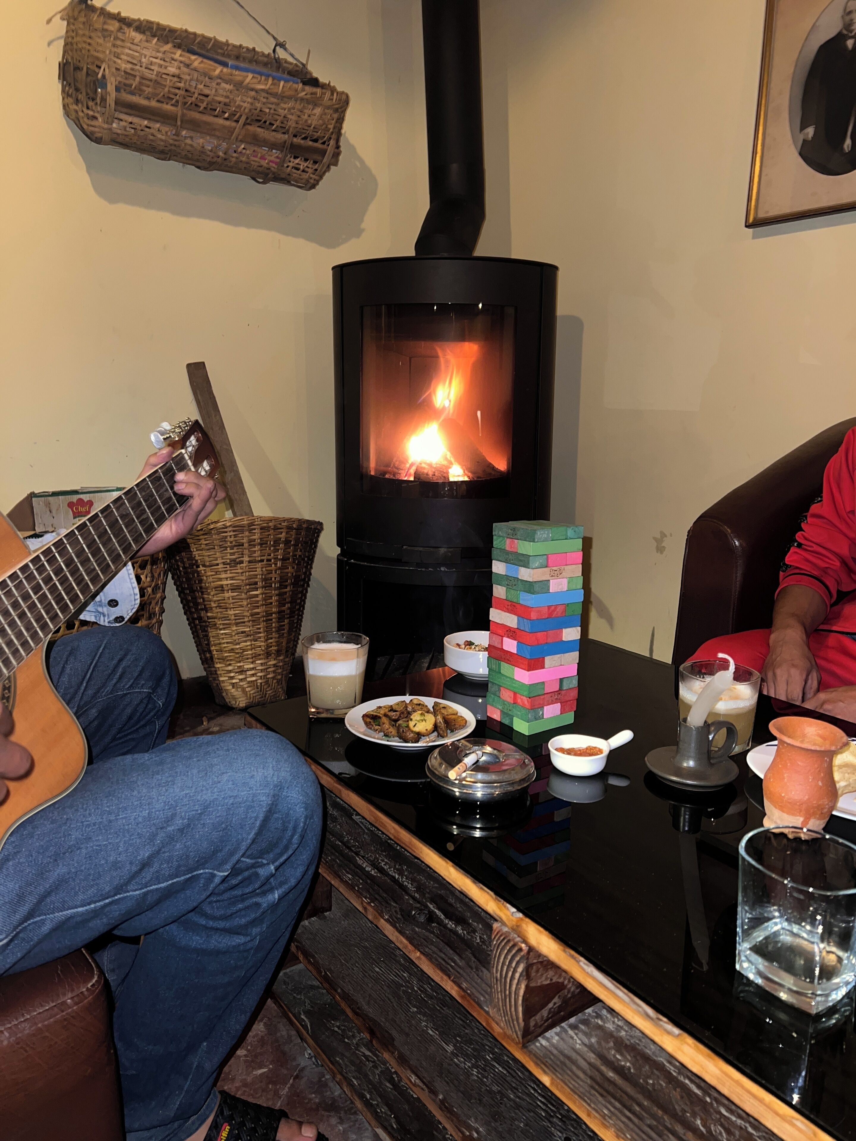 A cozy room with a wood-burning stove, a guitar, a plate of food, and a Jenga tower.