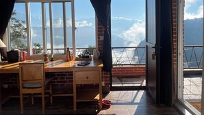 Una habitación con un escritorio de madera, una silla y vistas a montañas a través de amplias ventanas.