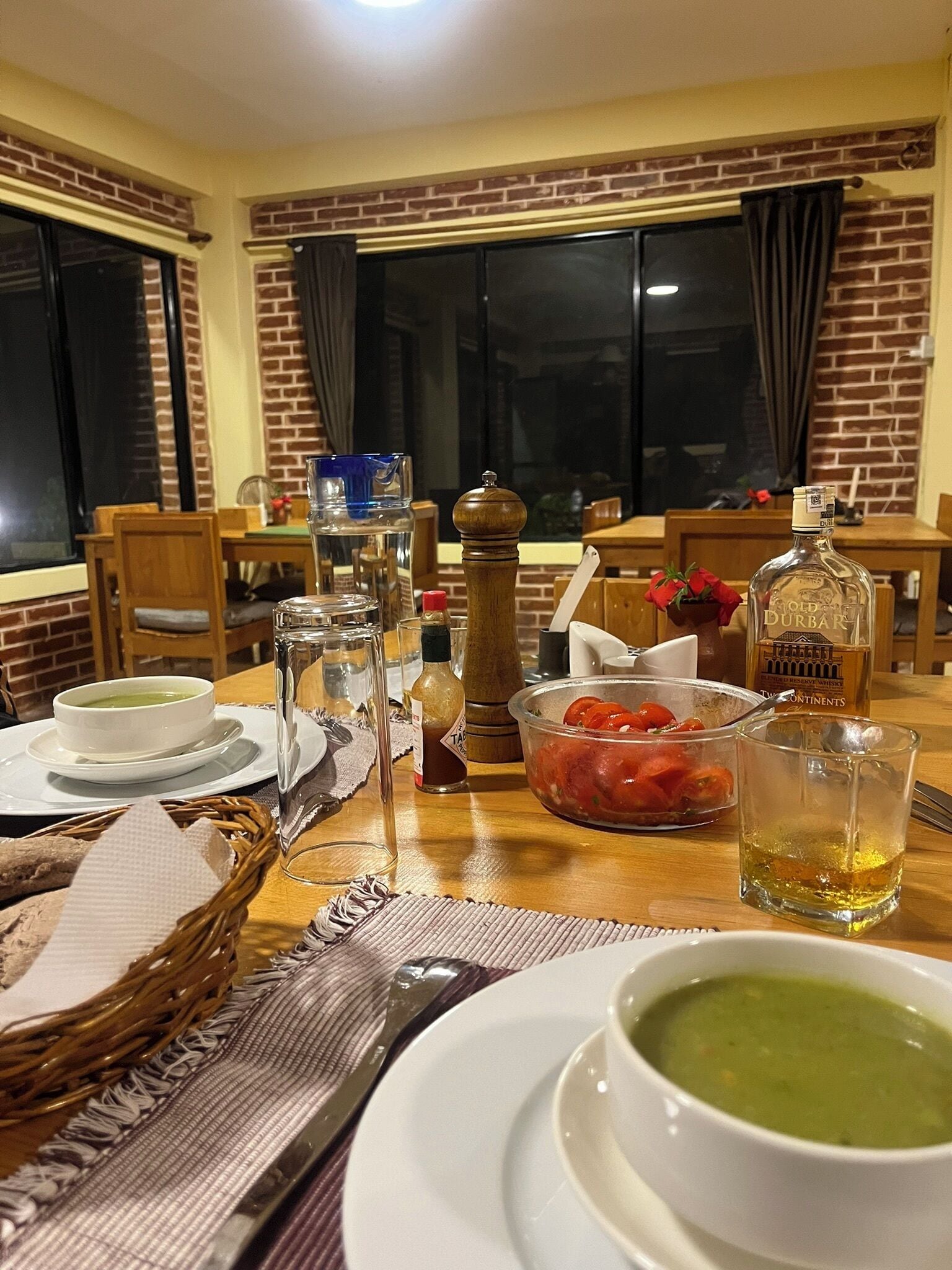 A dining table set with various dishes, including a bowl of soup, a glass of whiskey, and a bowl of tomatoes.