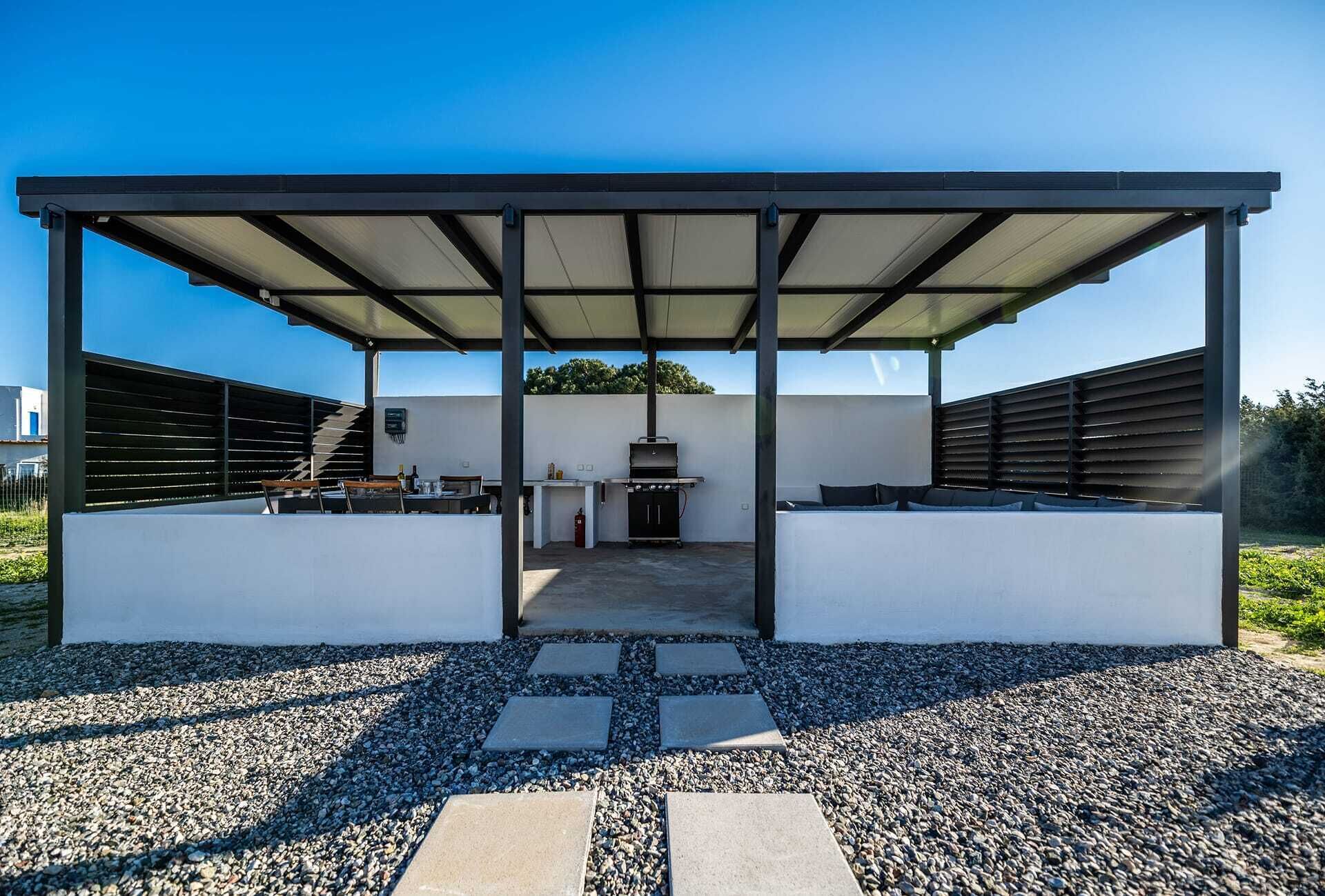 Un espacio de patio exterior techado con una parrilla, asientos y un paseo cubierto.