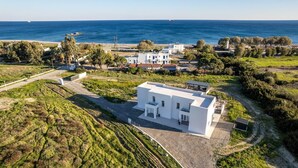 Een modern wit gebouw met een plat dak, omgeven door groen en een helder uitzicht op de zee.