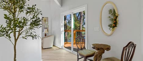 Ein Zimmer mit Holzboden, einem Esstisch mit Stühlen, einem Blumentopf und Blick durch eine Glastür auf einen Außenbereich.