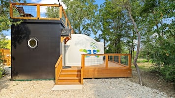 A small, enclosed structure with a wooden deck and a white wall featuring a colorful design.