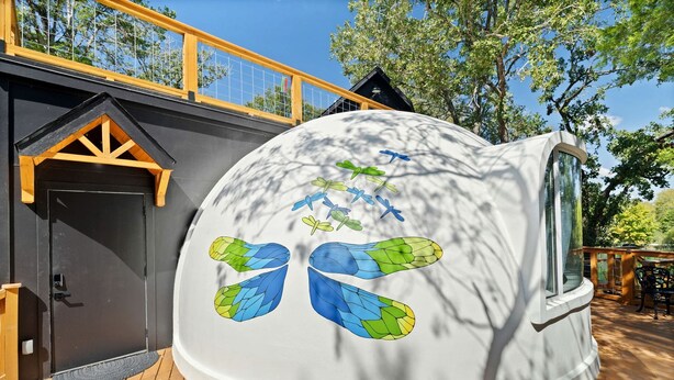 Una estructura abovedada con puerta y ventanas, rodeada por una terraza y árboles.