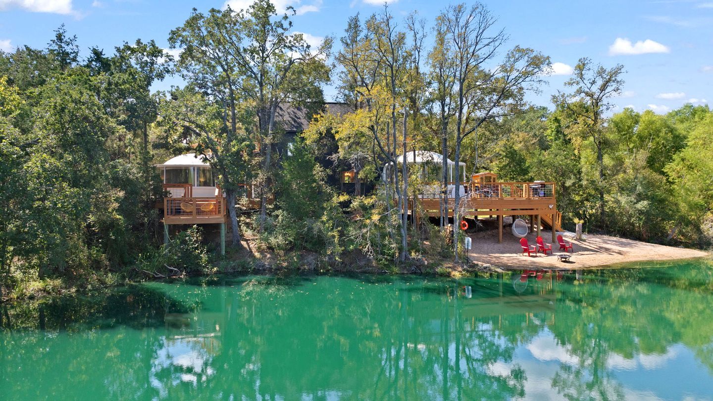 A cabin with a deck overlooking a body of water, surrounded by trees.