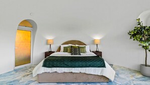 Un dormitorio con una cama, dos mesitas de noche, una lámpara, una planta y una puerta.