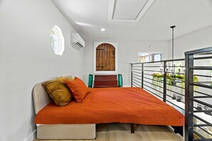 A bedroom with a bed, a wooden door, a window, and a balcony with a railing.