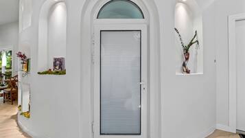 Un interior blanco con una puerta cerrada, un estante pequeño con una planta y un cuadro en la pared.