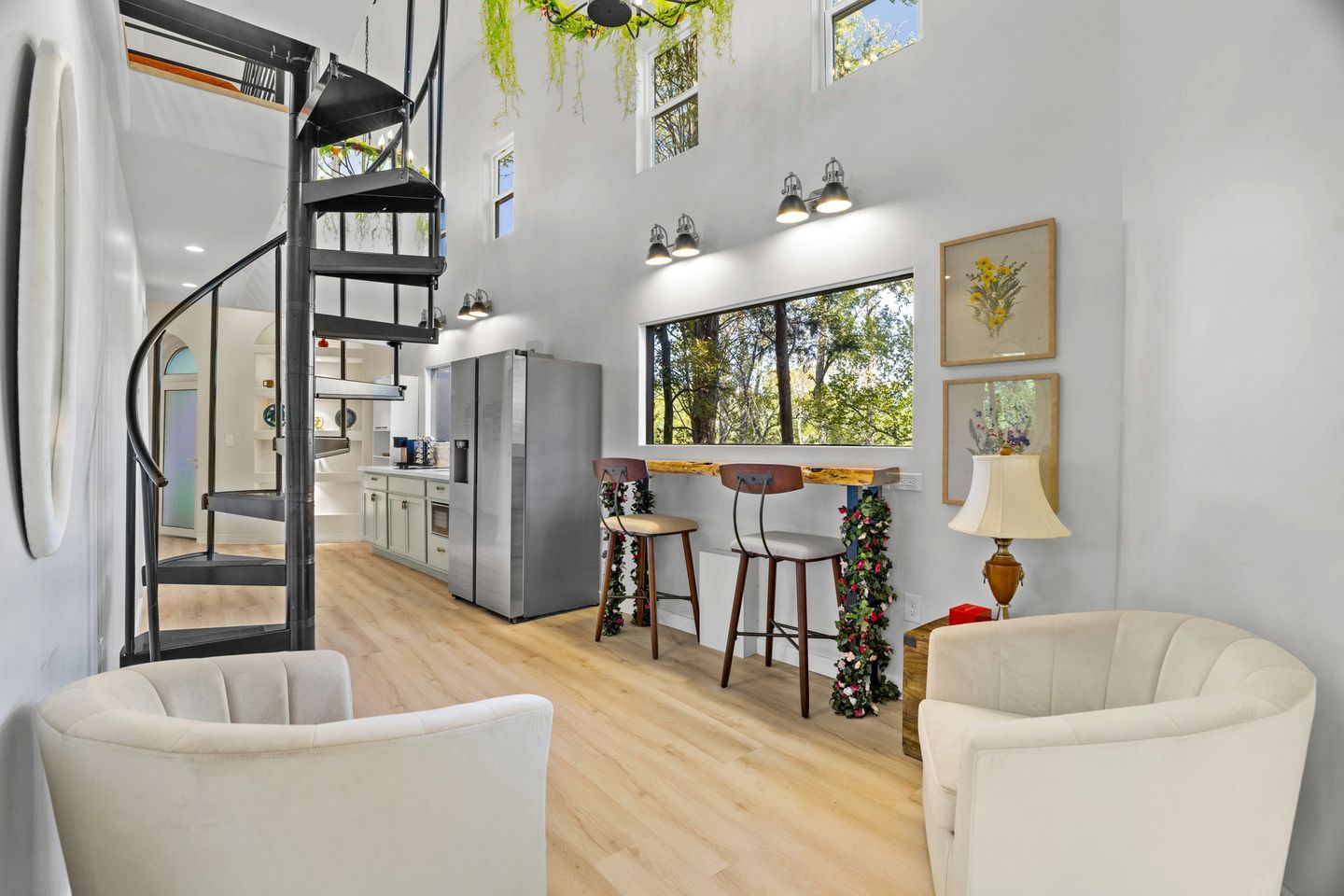 A modern kitchen with a spiral staircase, wooden flooring, and a dining area with two chairs and a table.