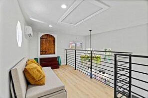 A modern interior with a wooden door, a sofa with a cushion, a staircase, and a balcony with a railing.