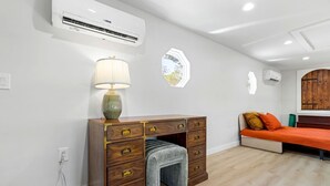 Una habitación con un aparador de madera, una lámpara, una cama con ropa de cama naranja y un aire acondicionado.