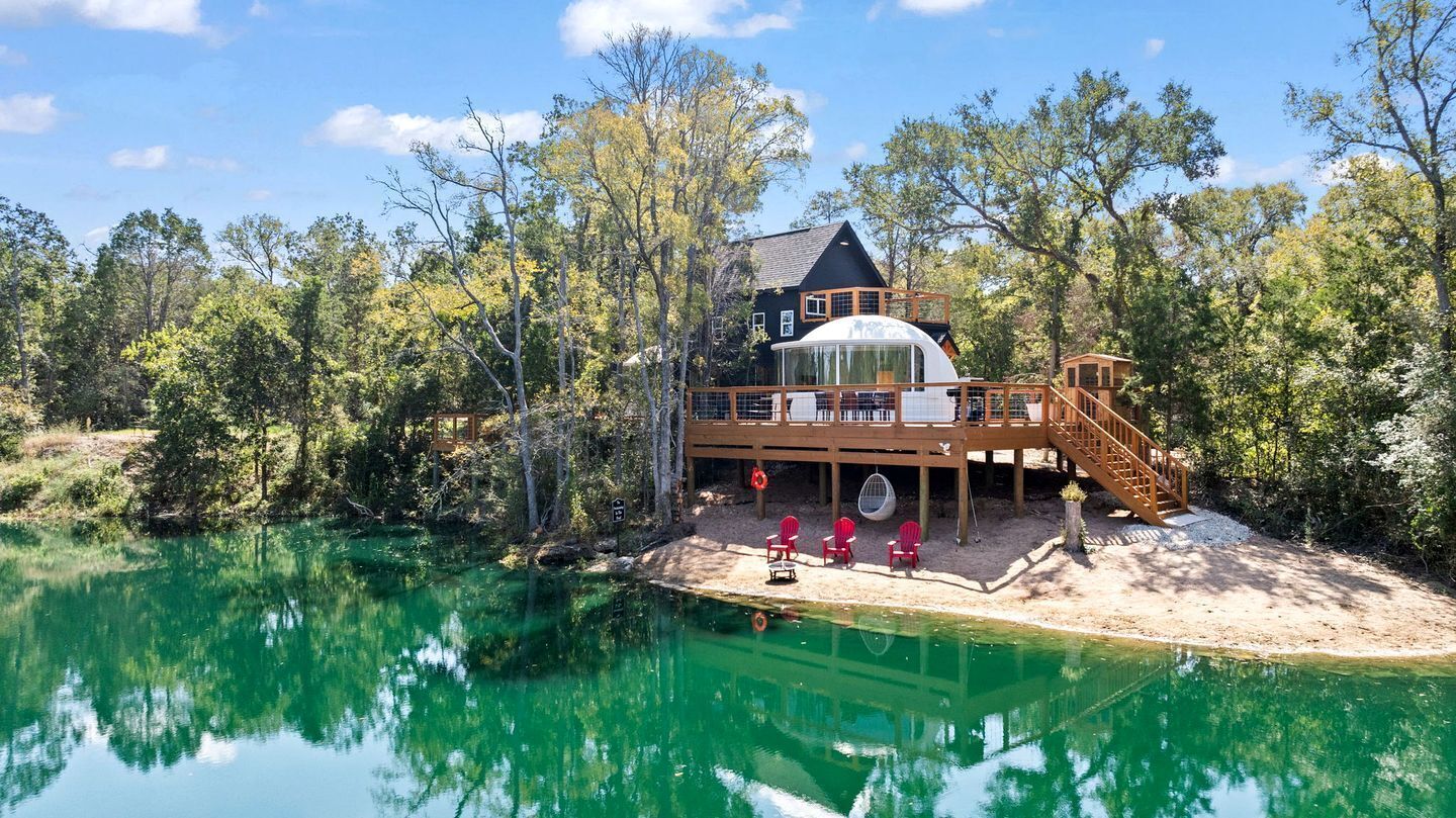 A lakeside cabin with a large deck, a covered outdoor area, and a swimming pool.