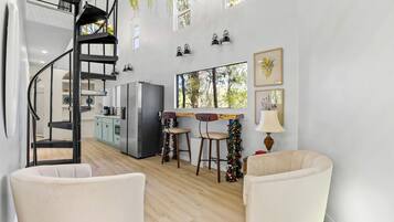 A modern kitchen with a built-in refrigerator, a dining area with two stools, a spiral staircase, and a large window.
