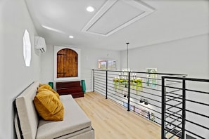 A modern interior with a wooden door, a sofa with a cushion, a staircase, and a balcony with a railing.