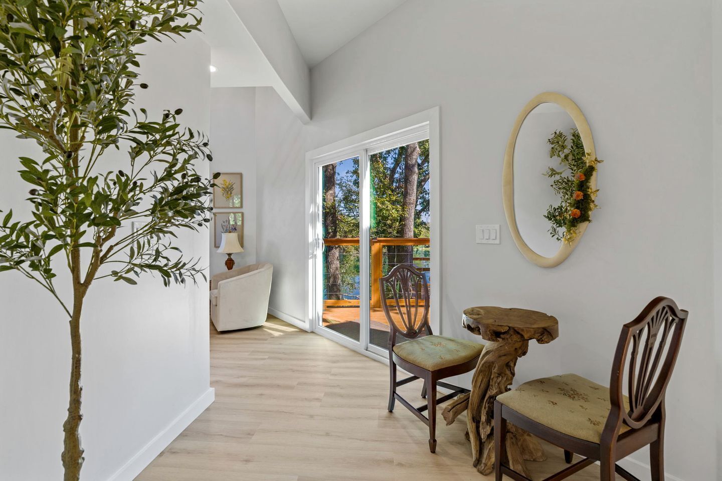 A room with a wooden floor, a dining table with chairs, a potted plant, and a view through a glass door to an outdoor area.