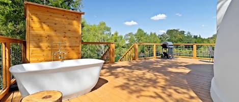 Una terraza de madera con una bañera blanca, una parrilla y una valla de madera.