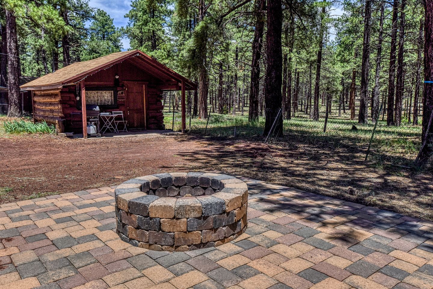 Uma cabana rústica com uma lareira de fogo em primeiro plano, cercada por uma área arborizada.