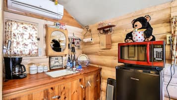 Eine kleine Küche mit einem Holzkorpus, einer Kaffeemaschine, einer Mikrowelle und einem Kühlschrank.