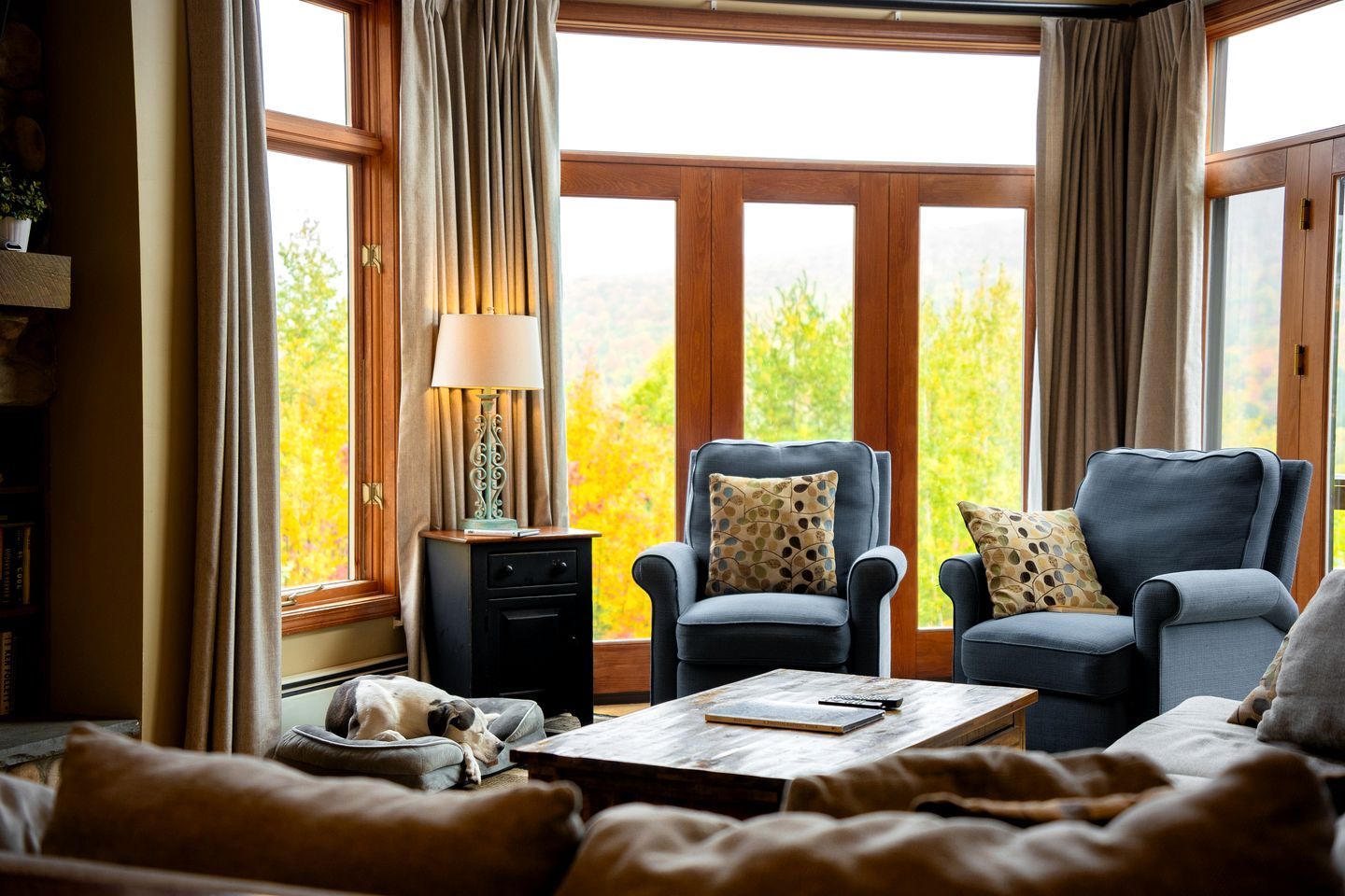 A cozy living room with a fireplace, two armchairs, a coffee table, and a dog bed.
