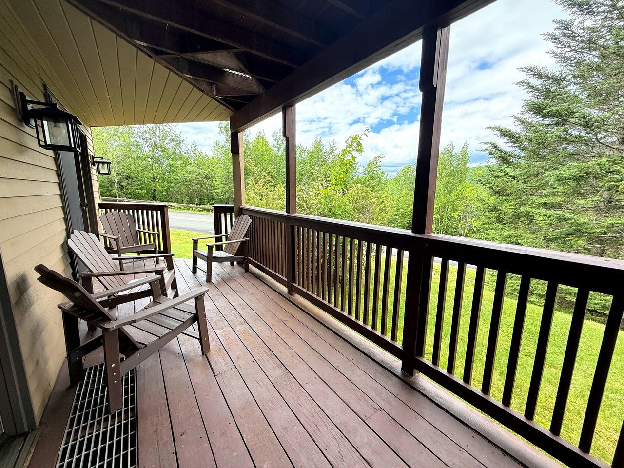 Ett trädäck med ett räcke, två Adirondack-stolar och utsikt över ett grönskande landskap.