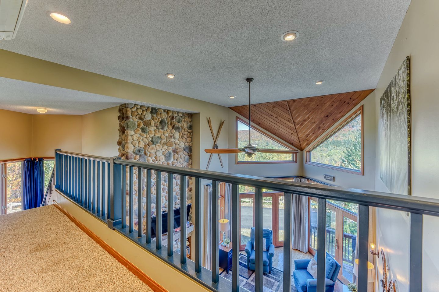 A spacious interior with a stone wall, a wooden ceiling, and a balcony with outdoor seating.