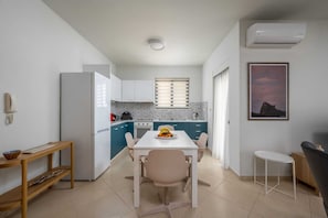 A compact kitchen with a dining area, a small table, a chair, and a single wall-mounted air conditioner. - Rodini Anassa | Aphrodite, Apartment (Rodos)