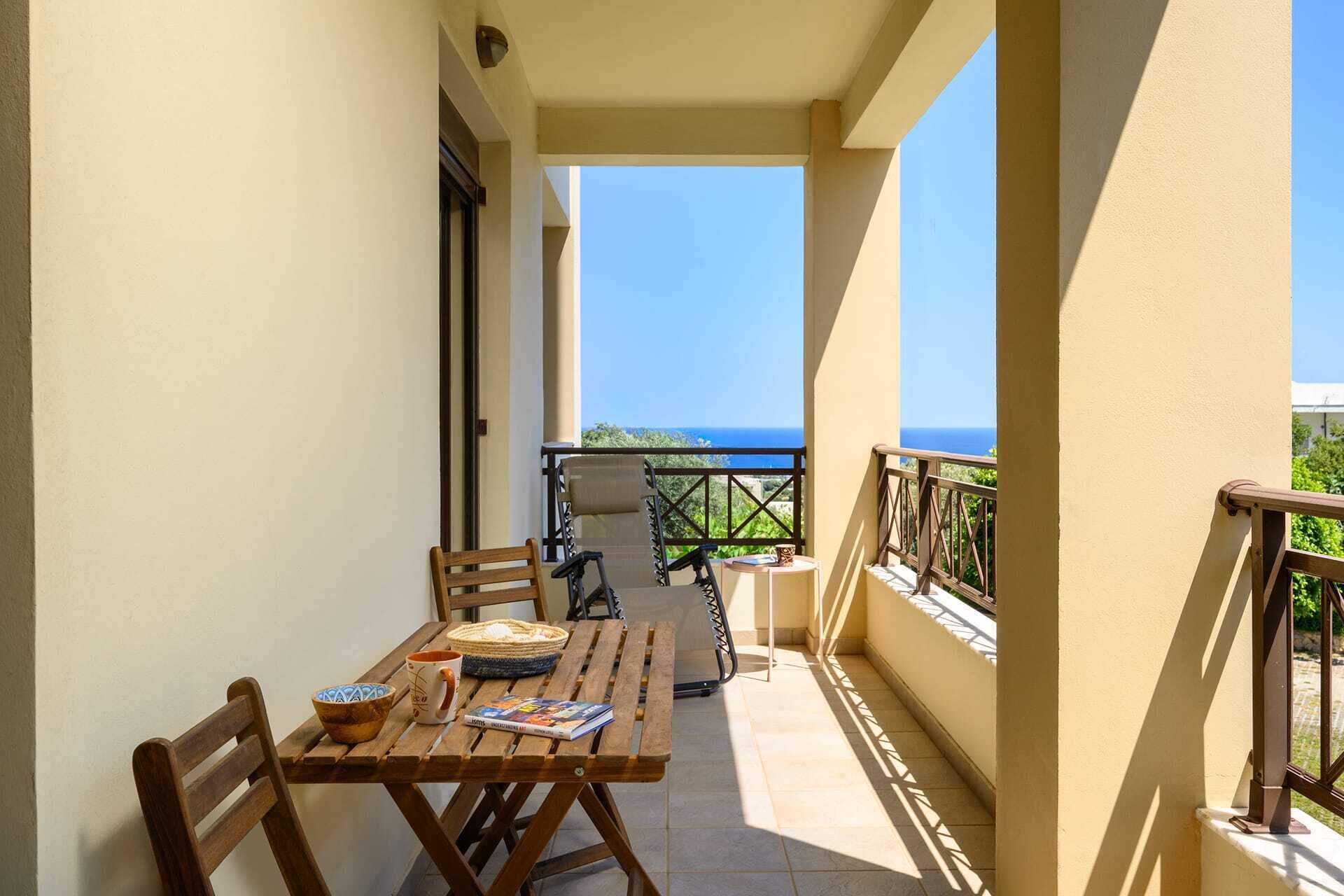 Ein Balkon mit Holztisch, Stühlen und Meerblick.