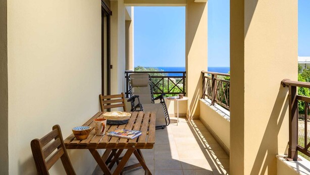 Un balcon avec une table en bois, des chaises et une vue sur la mer.