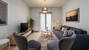 Un salon moderne comprenant un canapé, deux fauteuils, un téléviseur, une table basse et une grande fenêtre avec des rideaux.