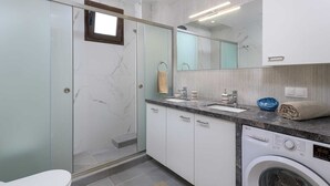 Een moderne badkamer met een douchecabine van glas, een ingebouwde wasmachine en een grote spiegel.