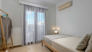 Een slaapkamer met een bed, een radiator, een raam met dunne gordijnen en een wandairconditioner.