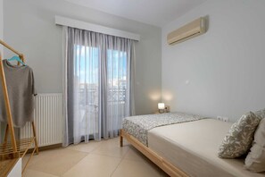 A bedroom with a bed, a radiator, a window with sheer curtains, and a wall-mounted air conditioner. - Rodini Anassa | Zeus, Apartment (Rodos)